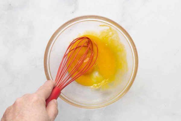A man's hand whisking egg yolks in a bowl.