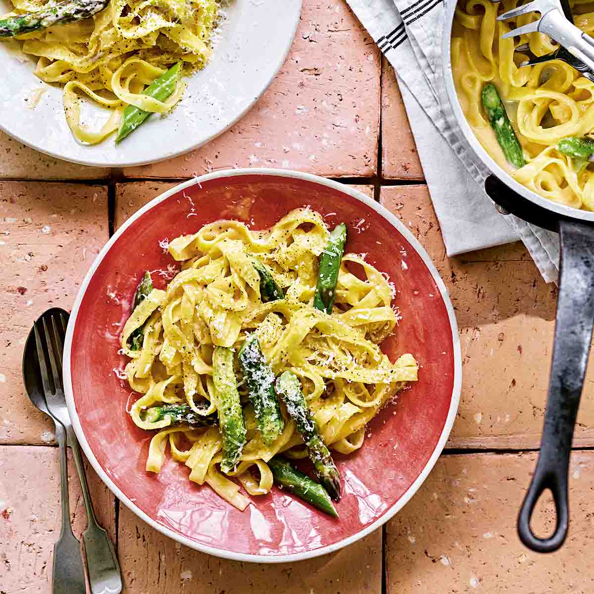 Two bowls filled with creamy asparagus pasta with a pot of pasta on the side.