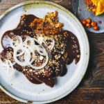 Two enchiladas de mole poblano on a white plate, topped with thinly sliced white onion.