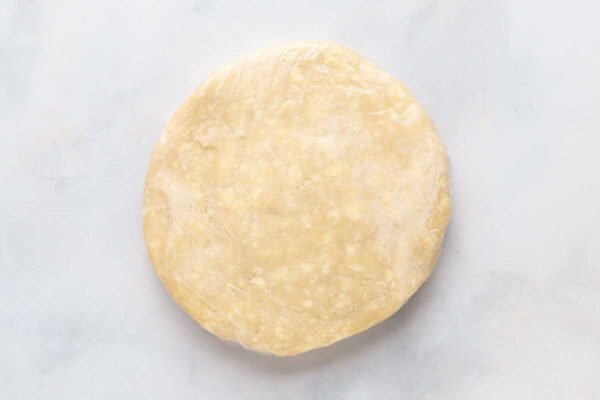 A round disk of pie dough wrapped in plastic.