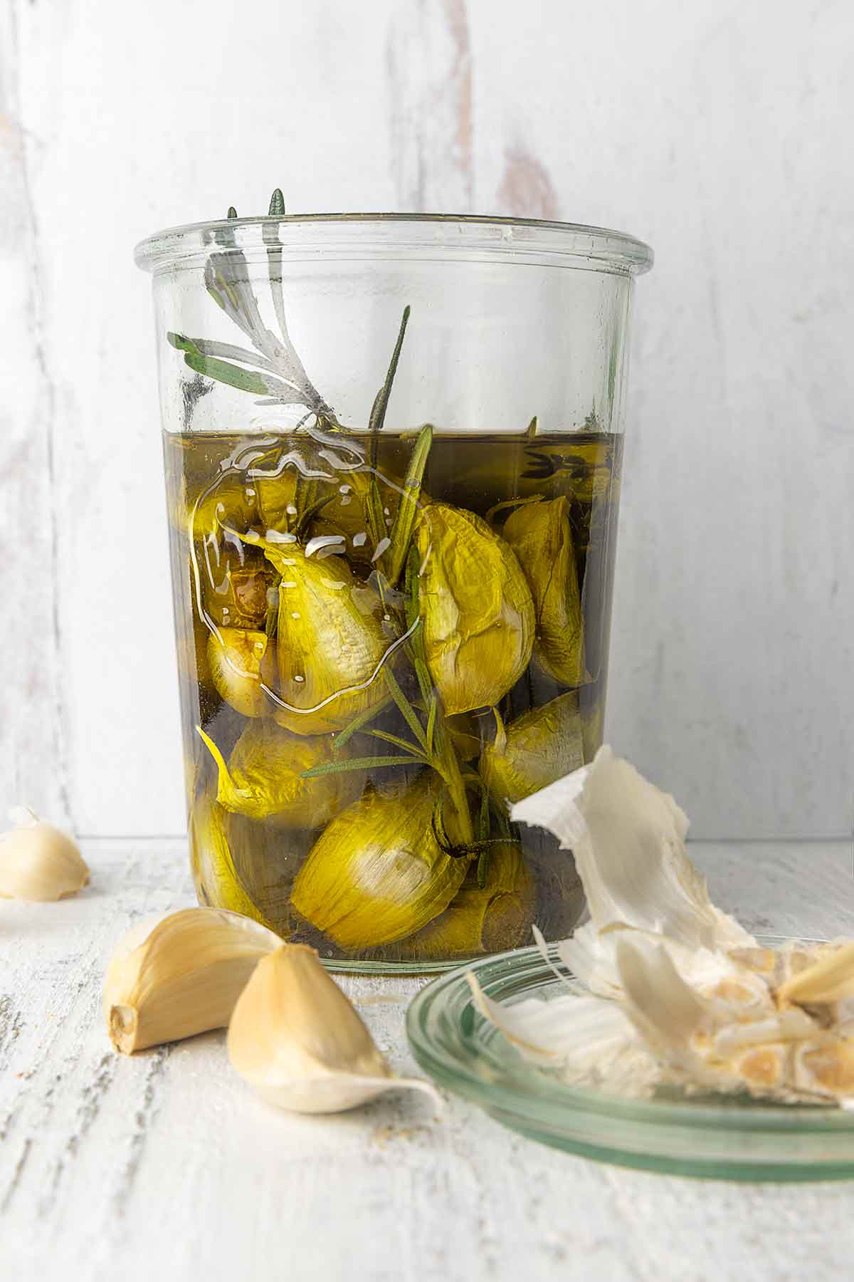 A jar of garlic confit with loose garlic cloves and husks nearby.