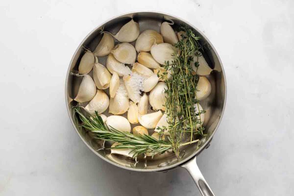 A pot filled with garlic cloves, thyme, and rosemary.
