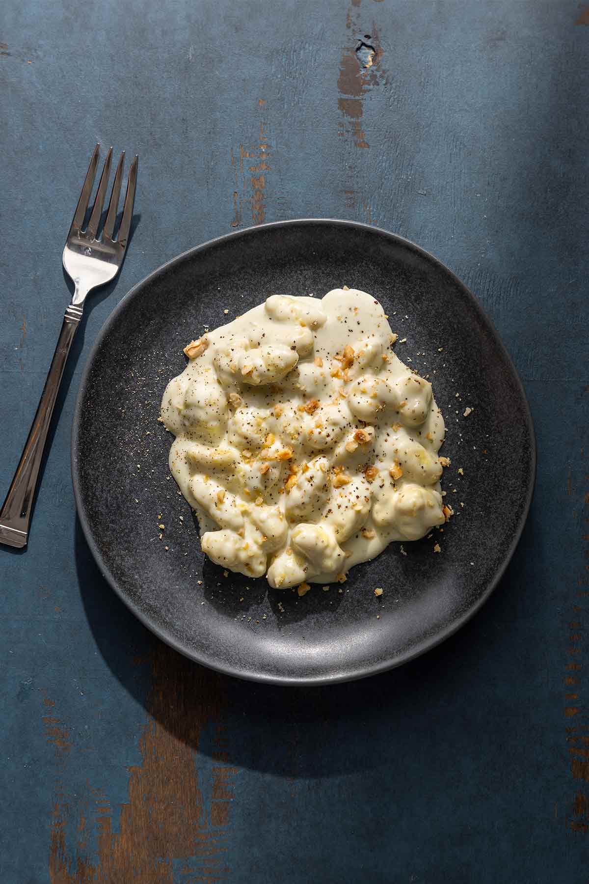 A portion of gnocchi with gorgonzola cream sauce sprinkled with chopped hazelnuts on a black plate.