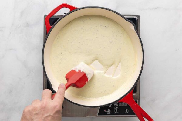 A person stirring blue cheese sauce in a skillet.