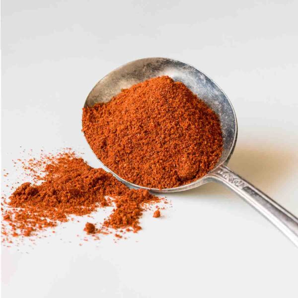 A large silver spoon holding a scoop of homemade chili powder with some spilled on the side.