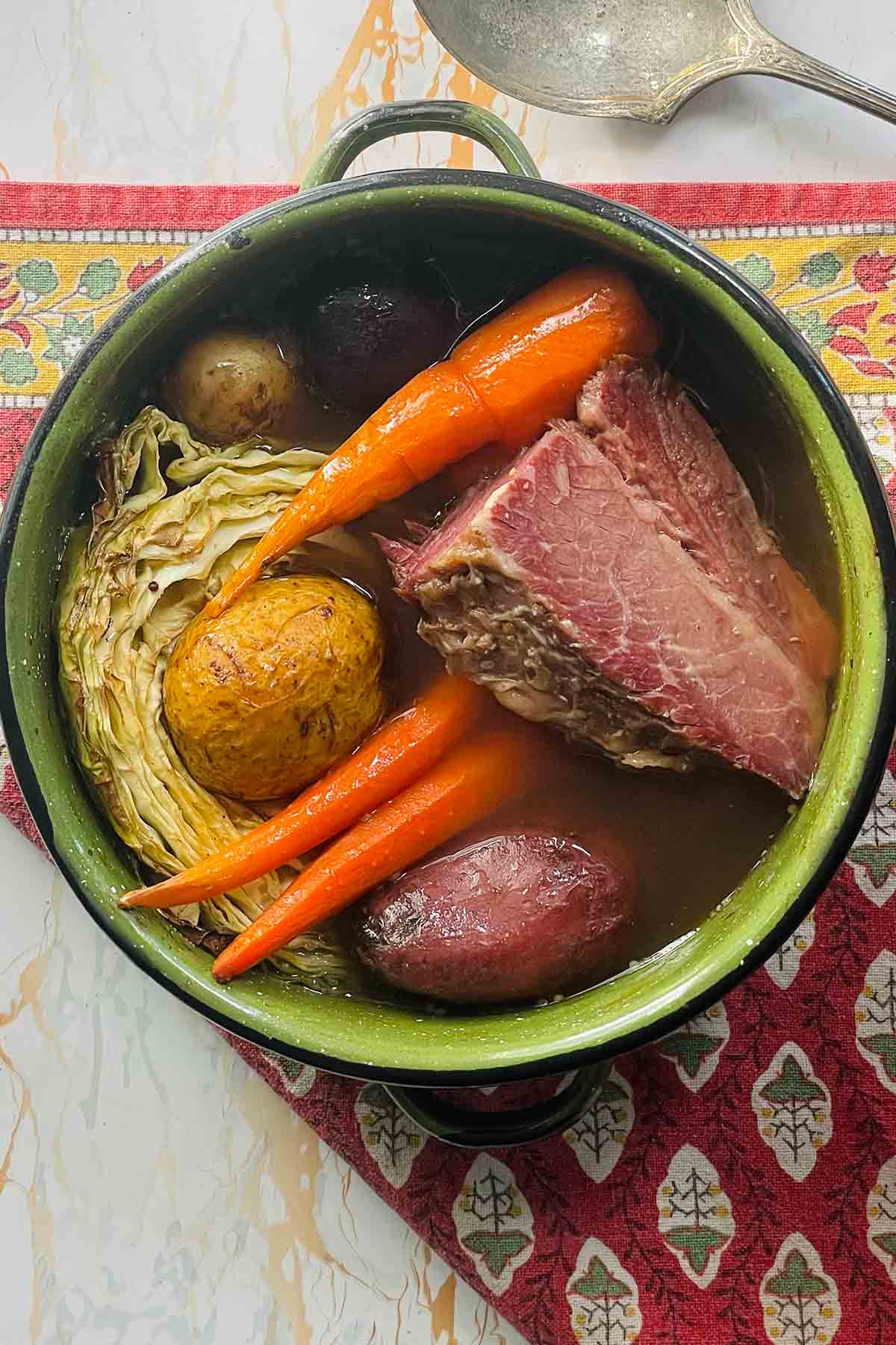A pot filled with a chunk of corned beef, three carrots, cabbage, and potatoes.