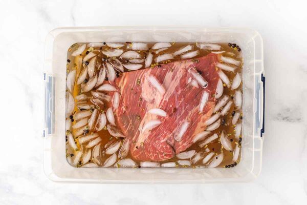A piece of brisket in a tub filled with brine and ice cubes.
