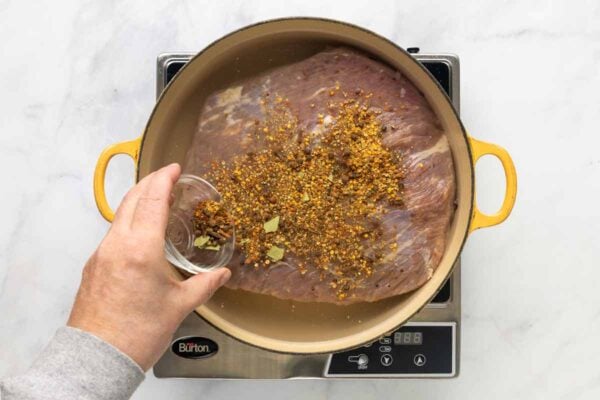 A person adding a spice mixture to corned beef in a Dutch oven.