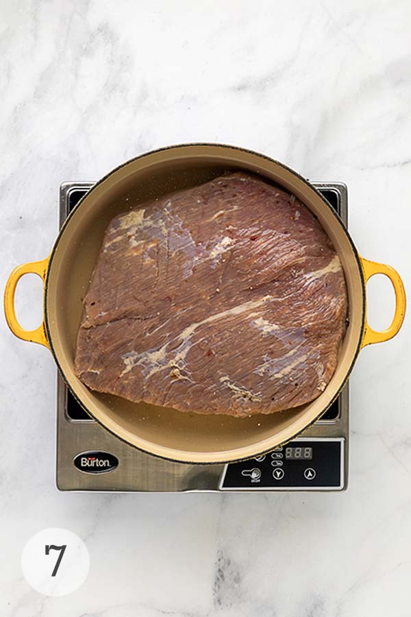 A Dutch oven filled with a cured corned beef brisket, simmering in water on the stovetop.