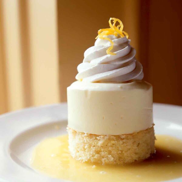 Lemon semifreddo in a pool of lemon sauce and garnished with a twist of lemon, sitting on a white dessert plate.