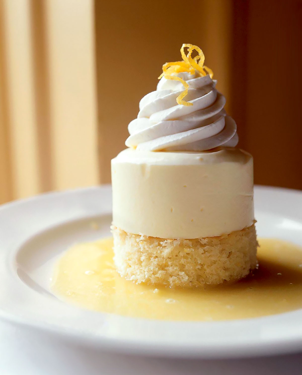 Lemon semifreddo in a pool of lemon sauce and garnished with a twist of lemon, sitting on a white dessert plate.