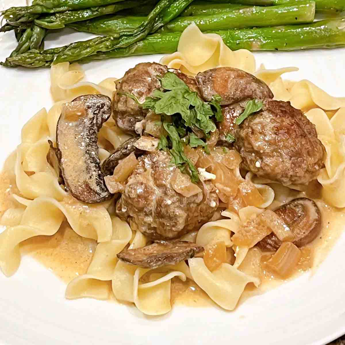 A plate of egg noodles topped with meatball stroganoff and asparagus on the side.