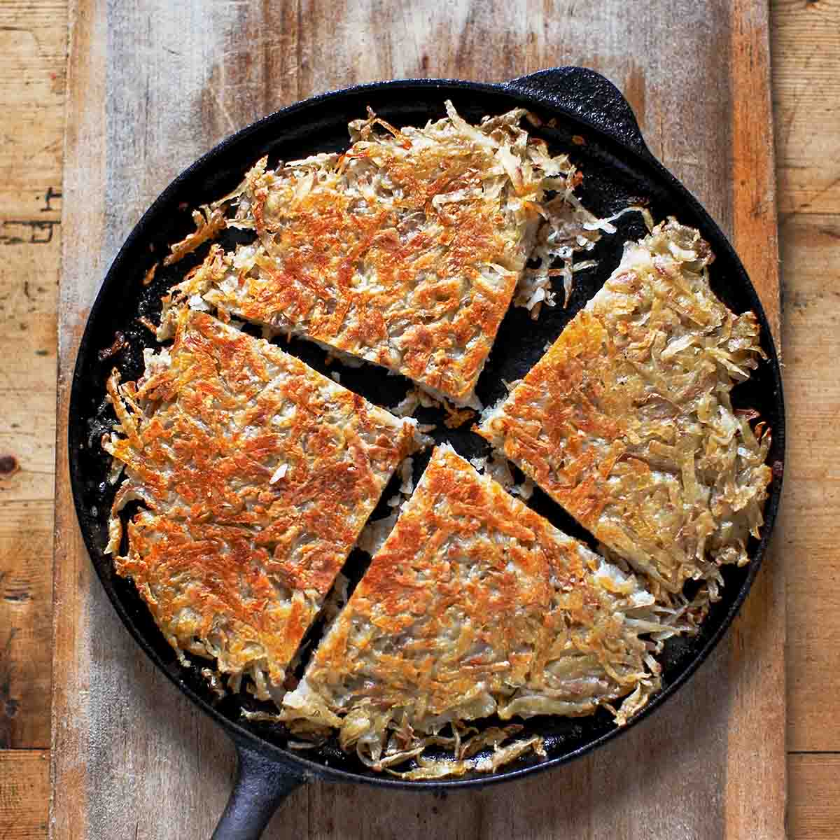 Cast iron skillet with a pan boxty (Irish potato pancake) in it, on a wooden cutting board.