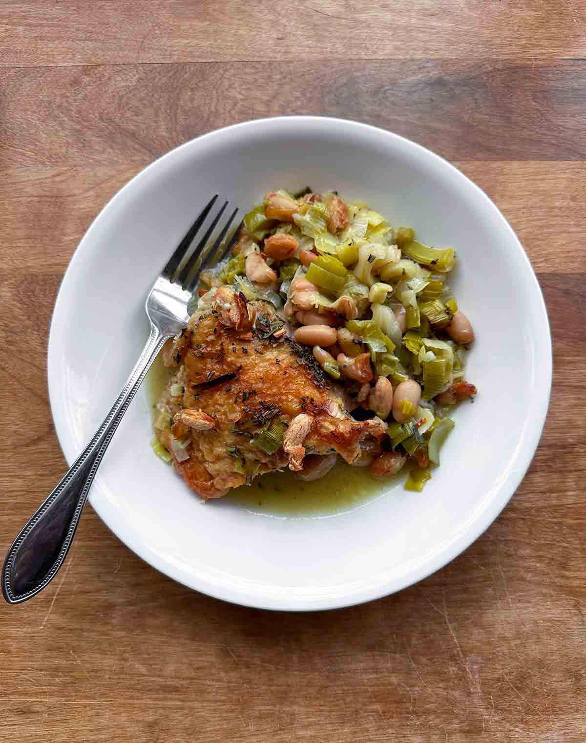 A piece of rosemary chicken with butter beans and leeks on a white plate.