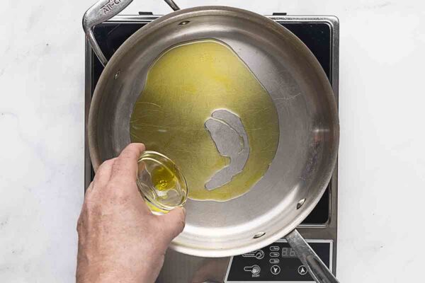 A person pouring olive oil into a skillet.