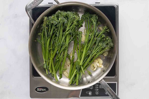 Broccolini and garlic slices in a metal skillet.
