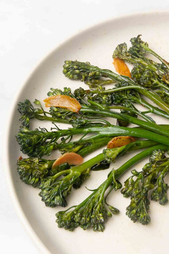 Seared broccolini and slices of browned garlic on a plate.