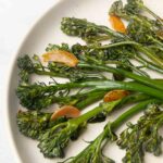 Seared broccolini and slices of browned garlic on a plate.