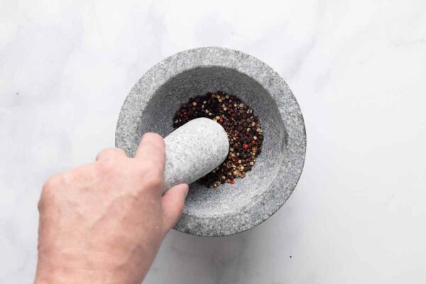 A person using a mortar and pestle to grind peppercorns.