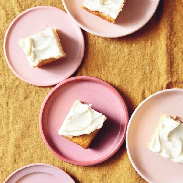 Individual servings of vanilla buttermilk cake with white frosting on pink plates.