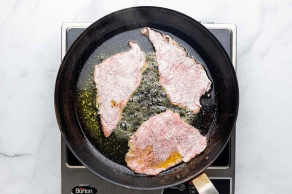 Veal scallopini being seared in butter and oil in a skillet.