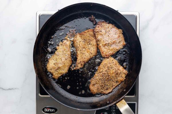 Browned pieces of veal scallopini in a skillet.
