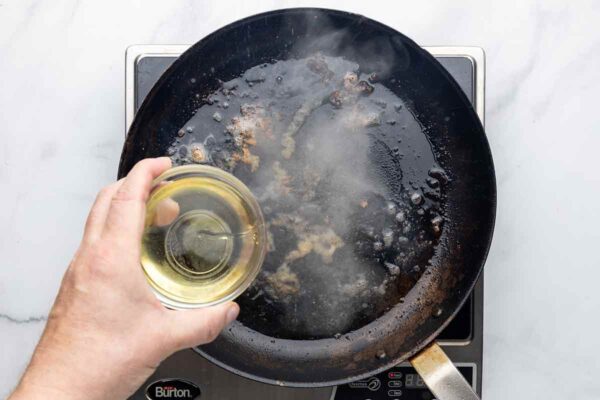 A person adding wine to a skillet.