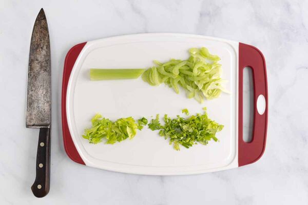 Sliced celery and chopped celery leaves on a cutting board.
