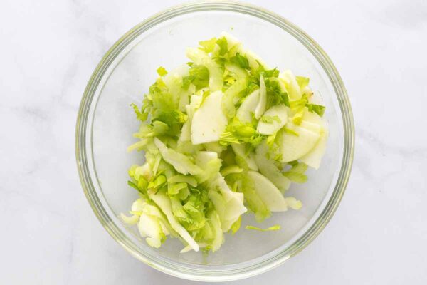 Celery slices, celery leaves, and apple slices in a glass bowl.