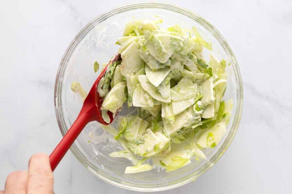 Celery and apples in a creamy dressing in a glass bowl.