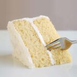 A slice of two-layer white cake with white frosting.
