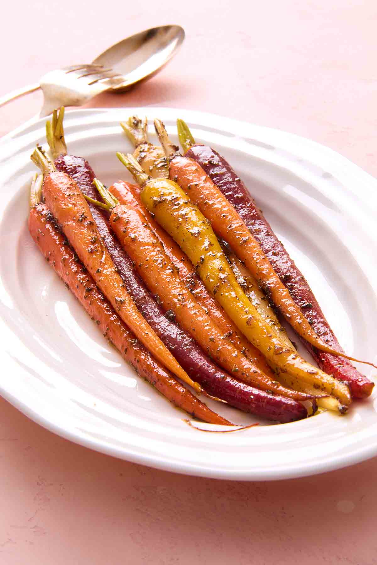 Nine colorful braised carrots on a white platter.