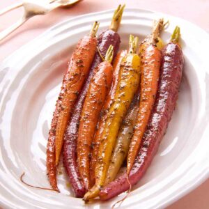 Nine colorful braised carrots on a white platter.