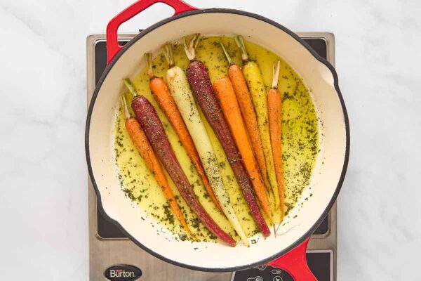 Nine peeled carrots in a skillet with oil and chopped fresh rosemary.