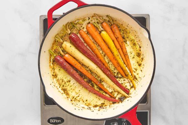 Nine braised carrots in a skillet with buttery rosemary sauce.