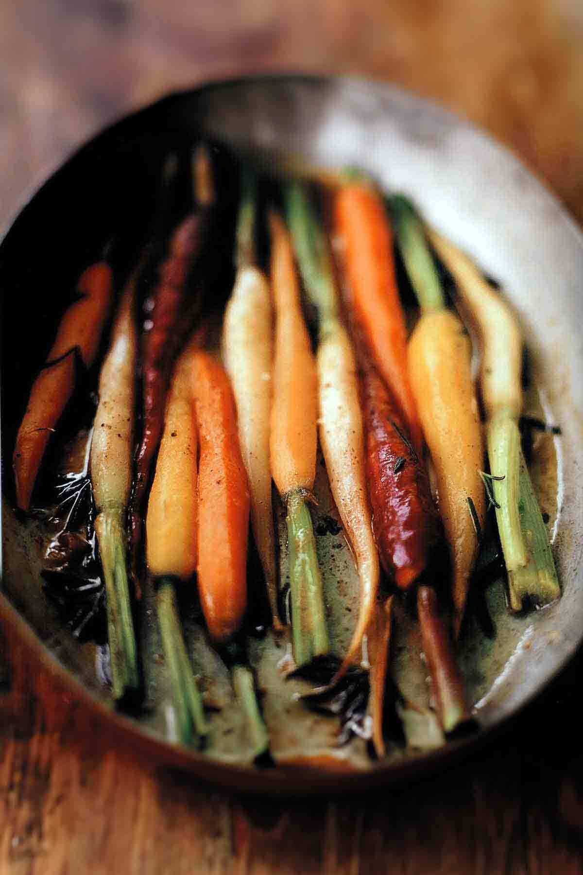 An oval dish with a dozen multi-colored carrots in braising liquid.