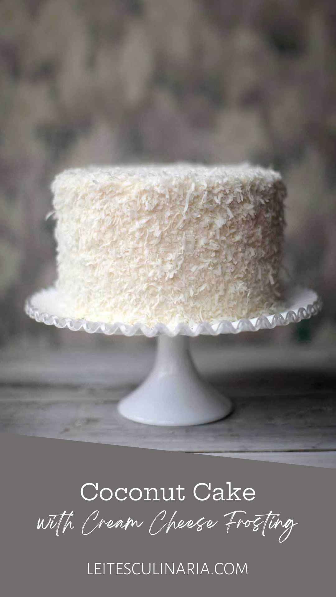 A coconut cake covered in shredded coconut on a white cake stand.