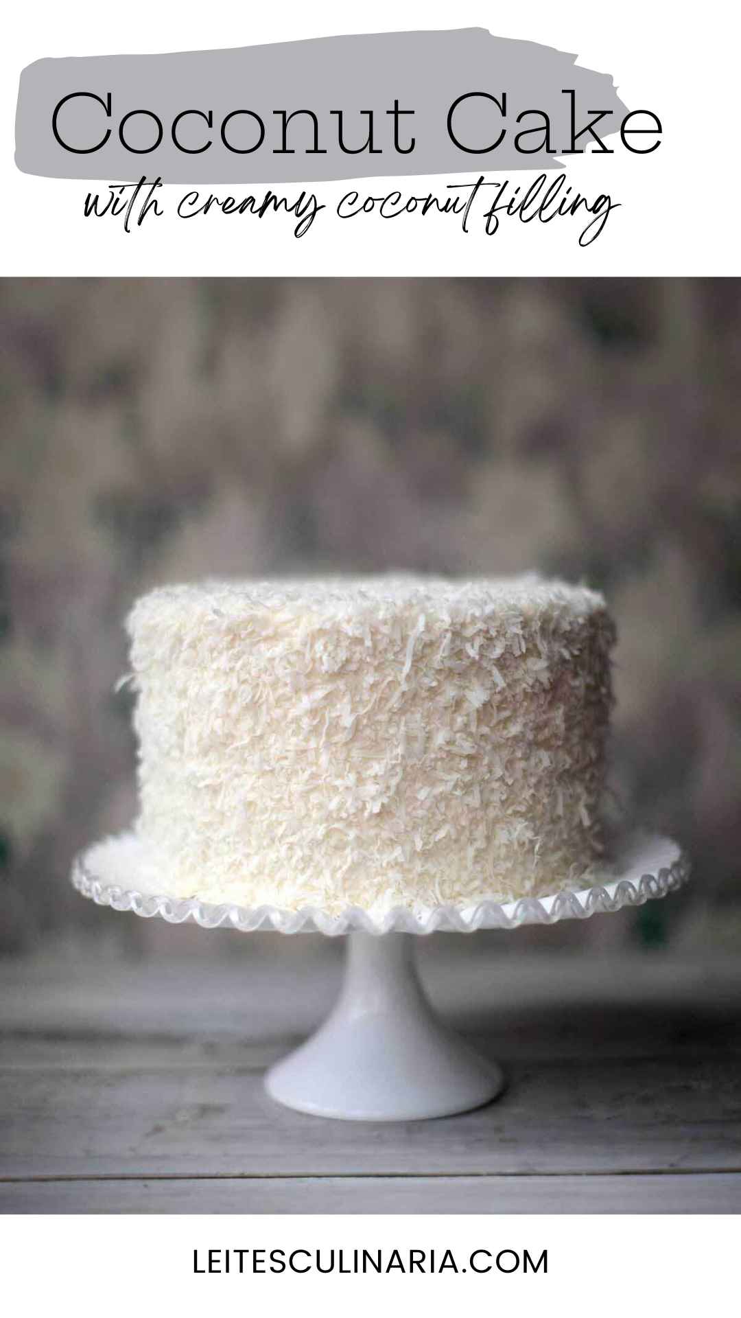 A coconut cake covered in shredded coconut on a white cake stand.