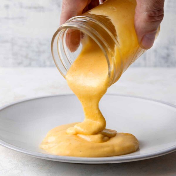 A person pouring Cheddar cheese sauce from a jar into a shallow bowl.