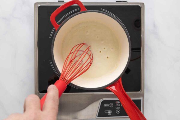 A person whisking a roux in a saucepan.