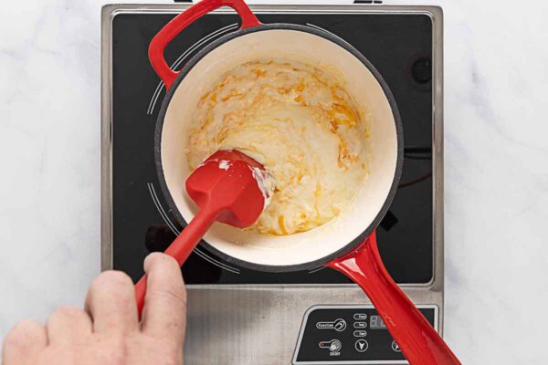 A creamy cheese sauce mixture being stirred in a saucepan.