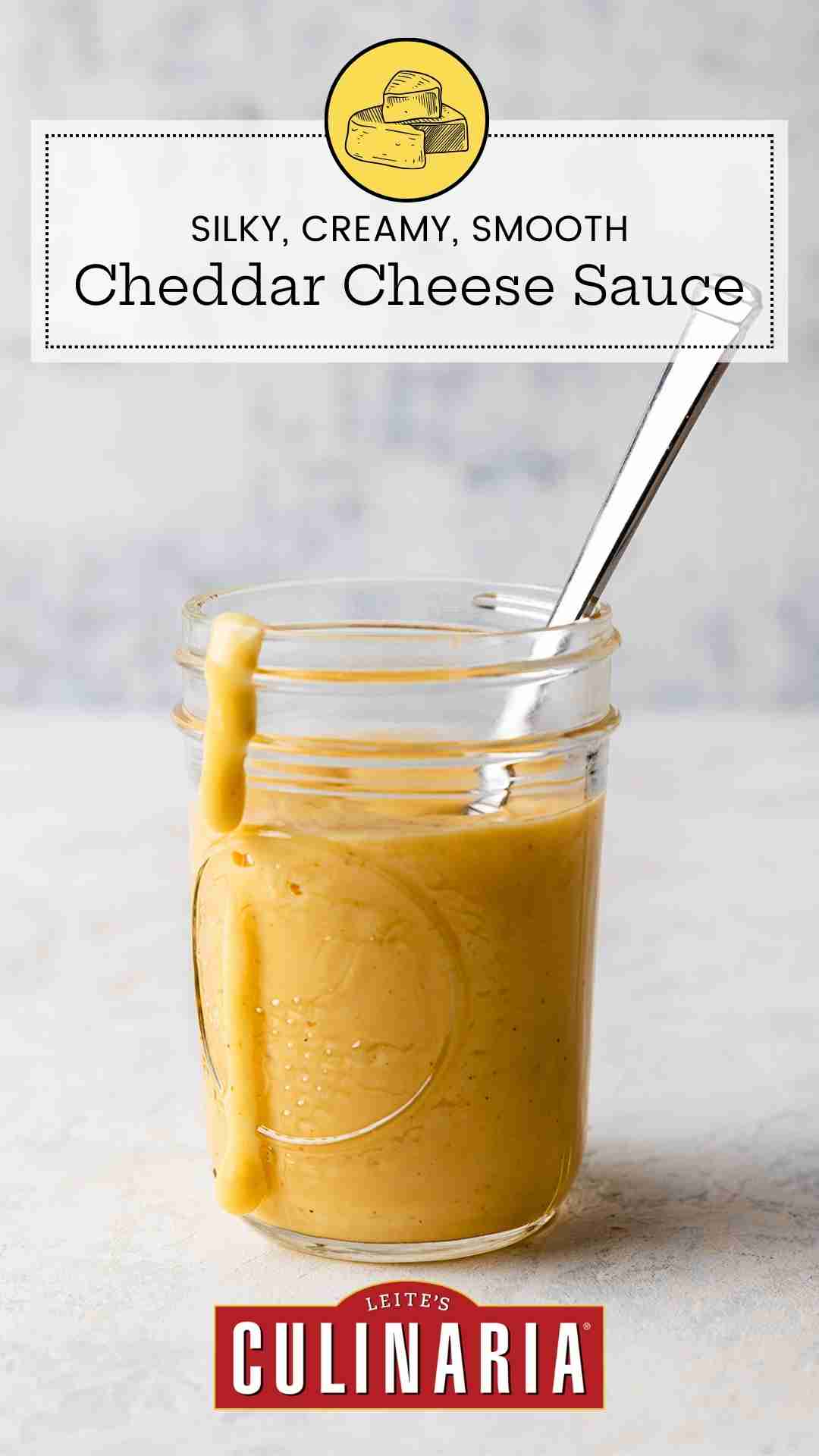A Mason jar filled with homemade Cheddar cheese sauce with a spoon resting inside and a drip of sauce down the side of the jar.