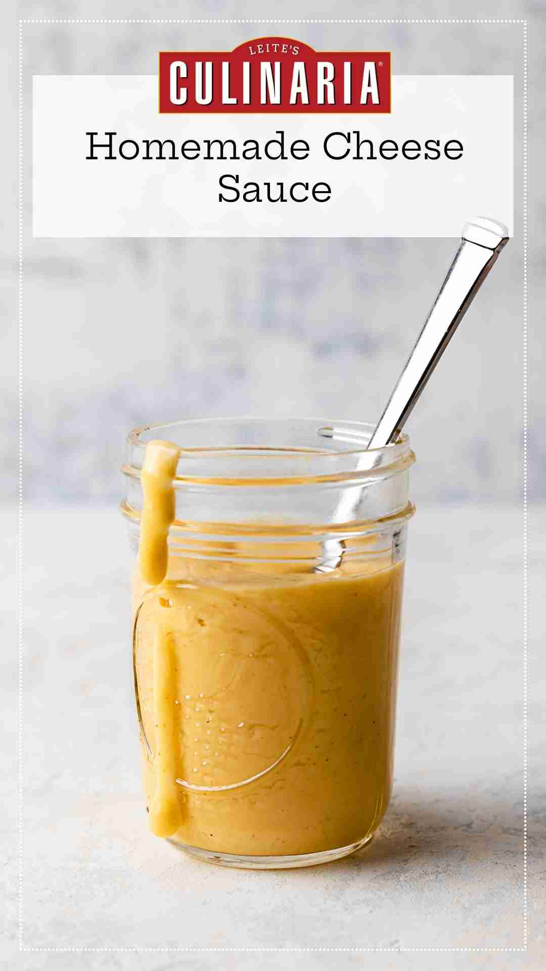 A Mason jar filled with homemade Cheddar cheese sauce with a spoon resting inside and a drip of sauce down the side of the jar.