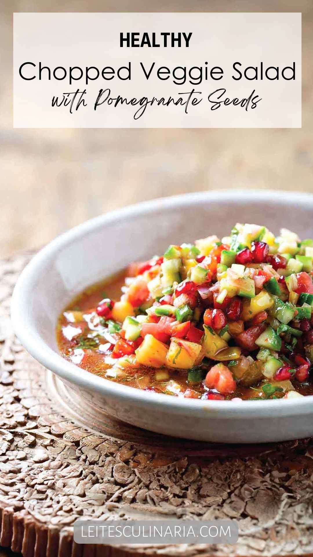 A white bowl filled with chopped vegetable salad with pomegranate seeds scattered on top.