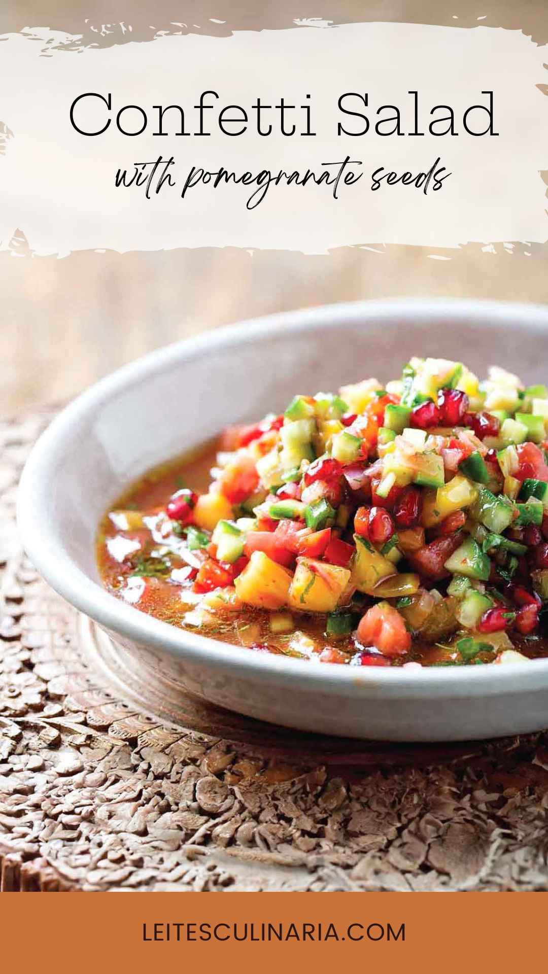 A white bowl filled with chopped vegetable salad with pomegranate seeds scattered on top.