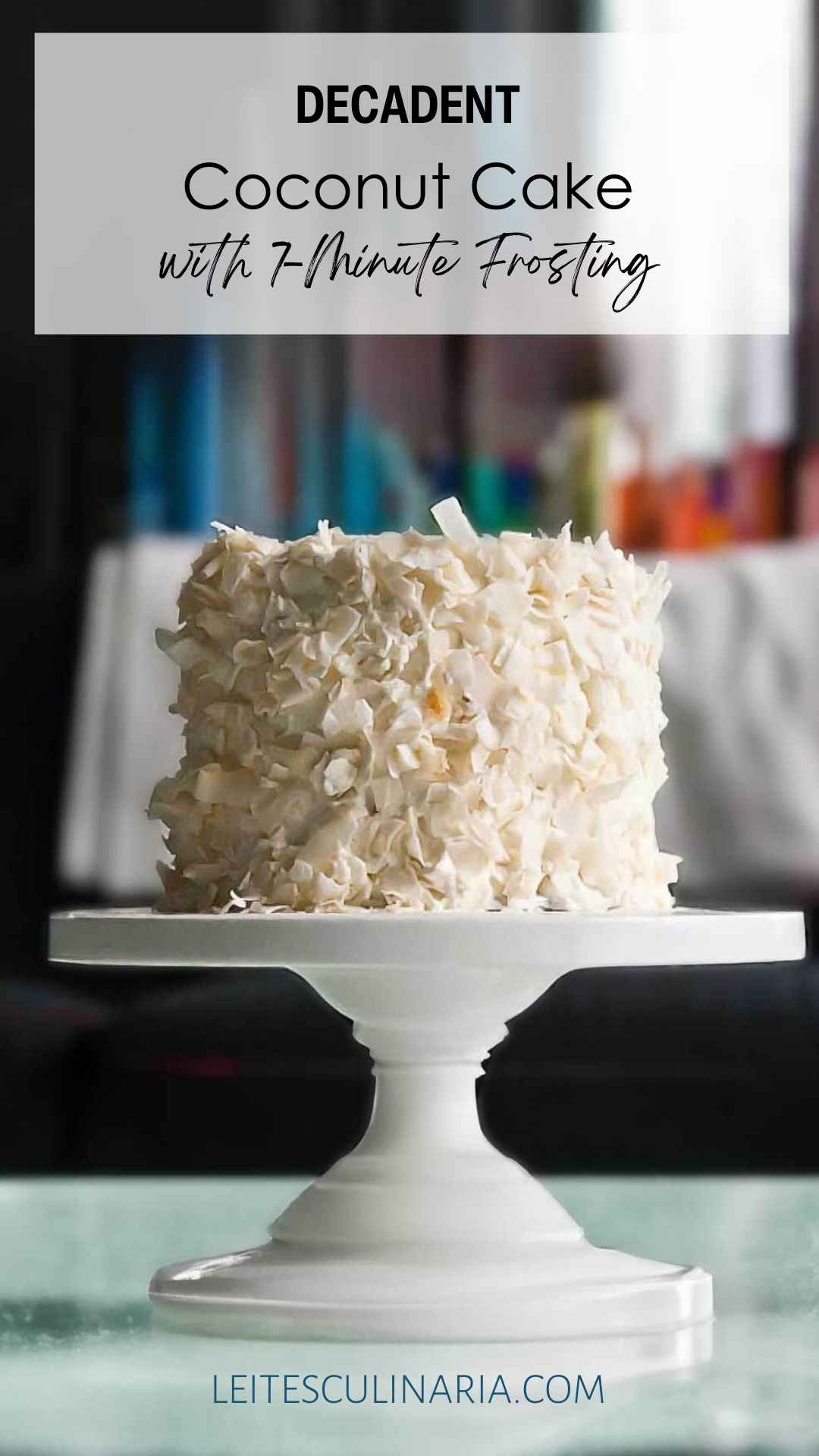 A coconut cake covered in flakes of coconut on a white cake stand.