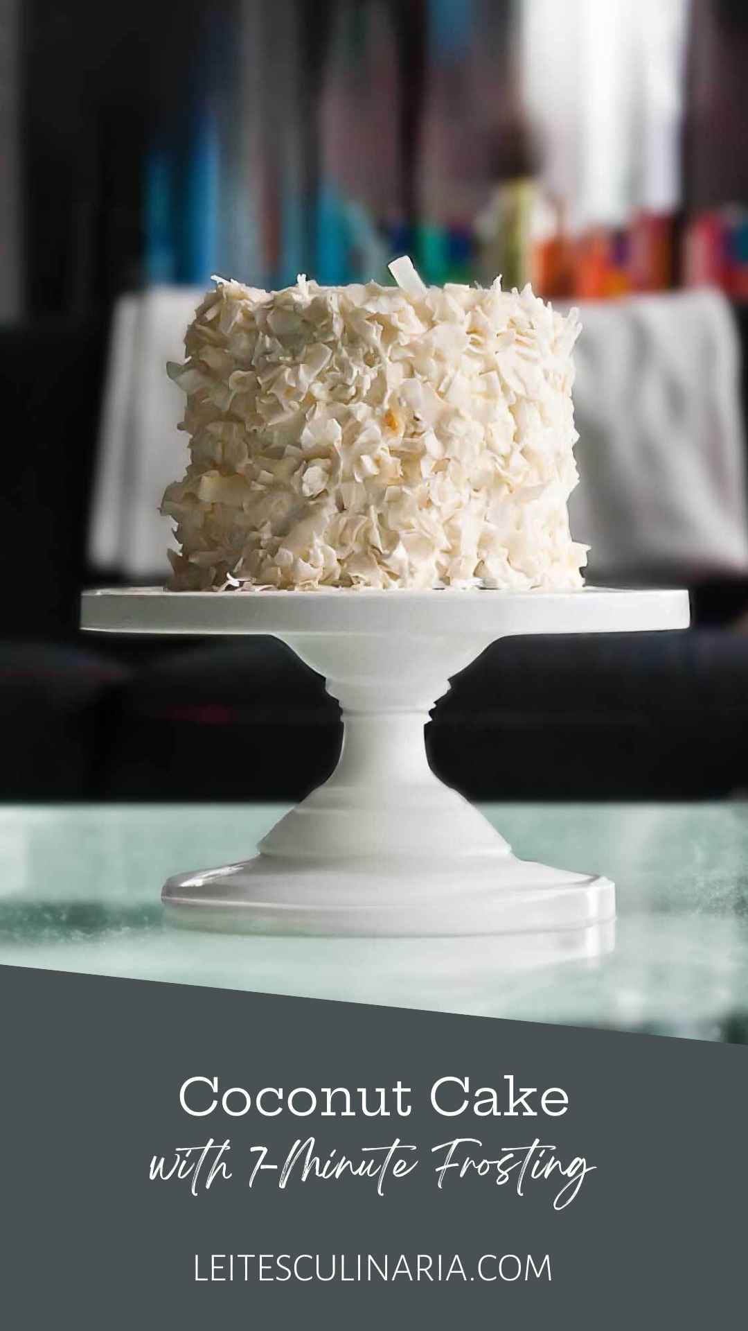A coconut cake covered in flakes of coconut on a white cake stand.
