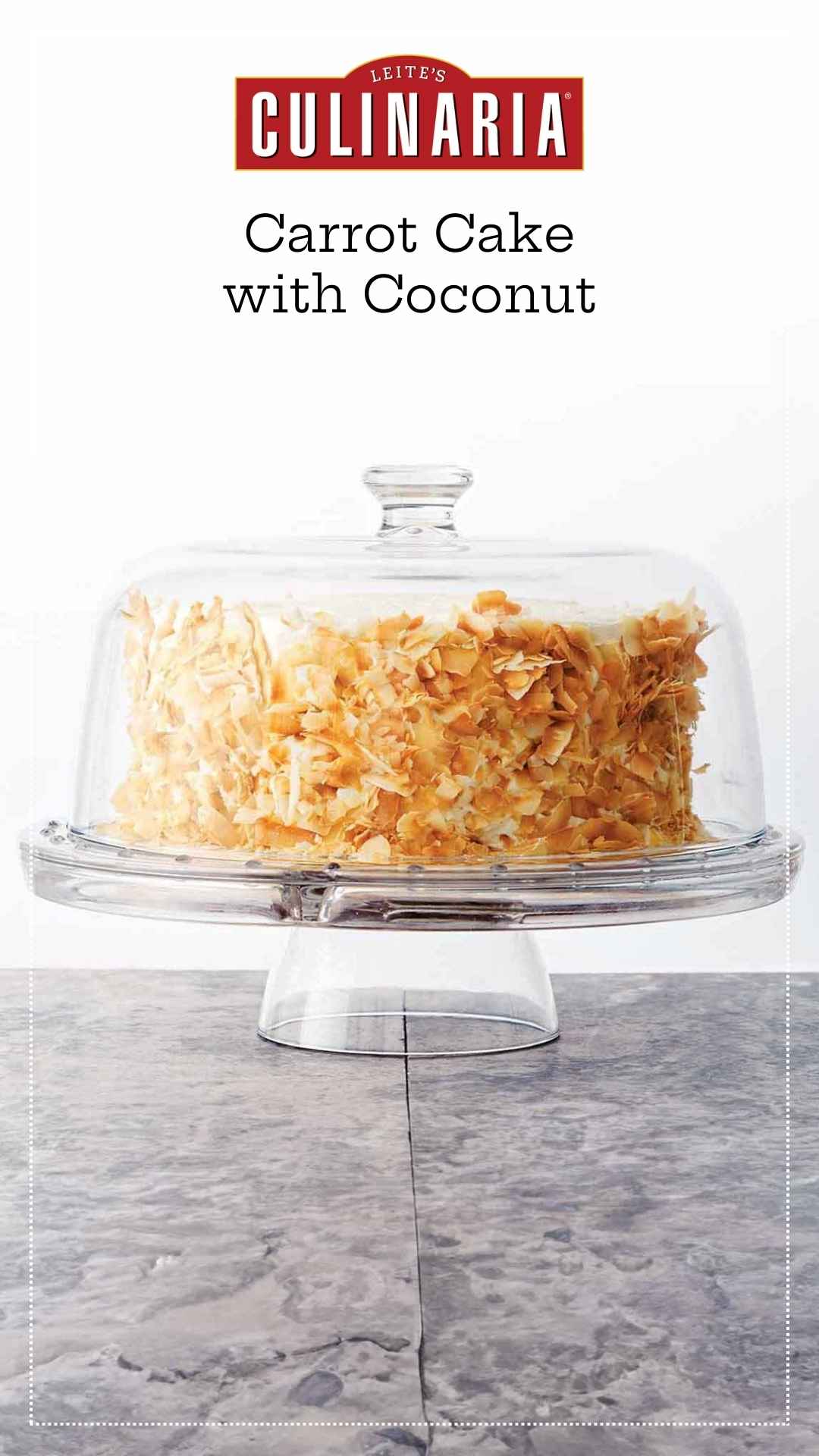 A carrot cake covered in toasted coconut flakes on a glass cake stand, covered with a glass dome.