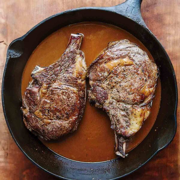Two seared ribeye steaks in a Guinness beer sauce in a cast iron skillet.