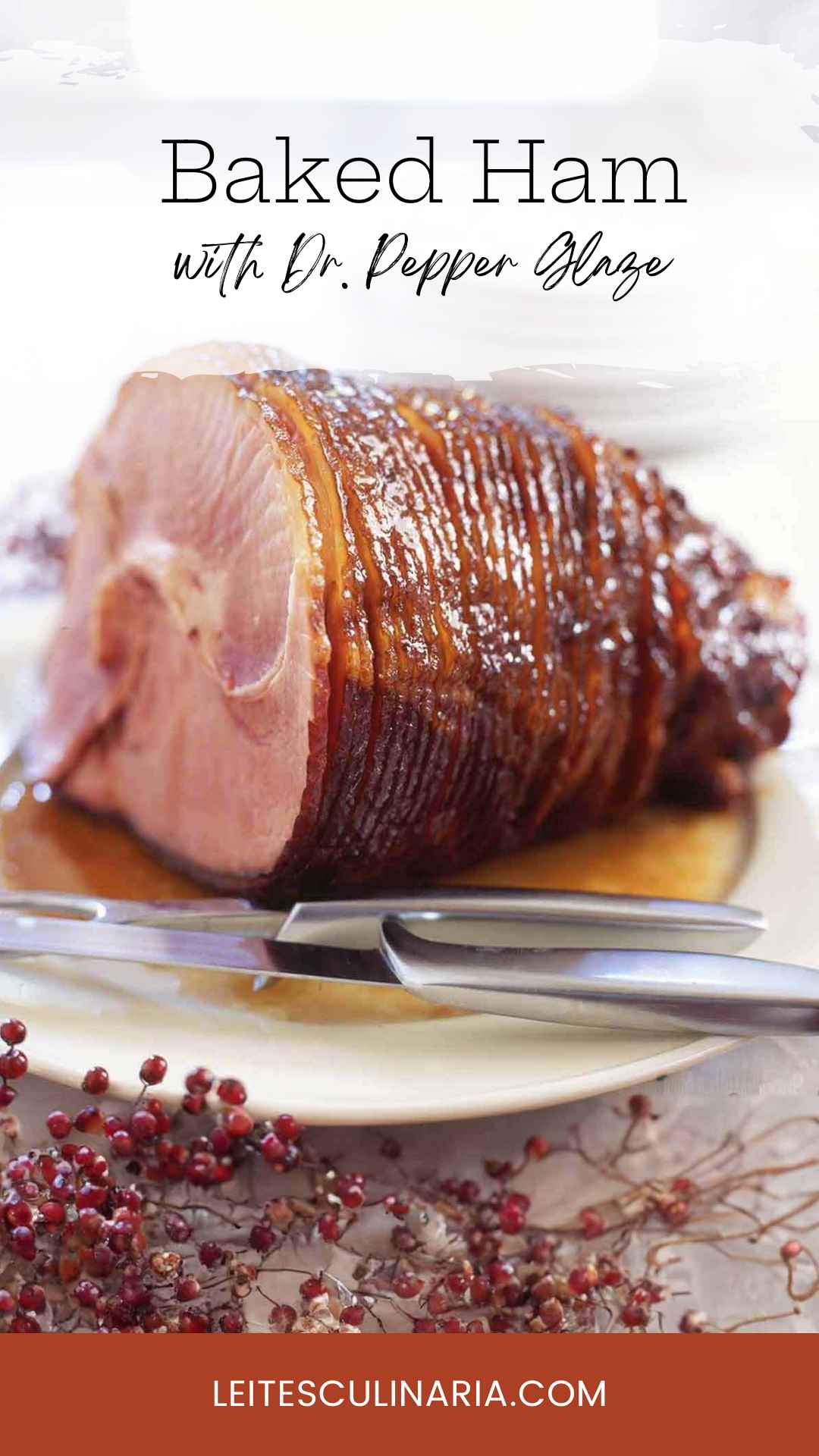 A glazed spiral cut ham on a white platter with a carving knife and fork nearby.